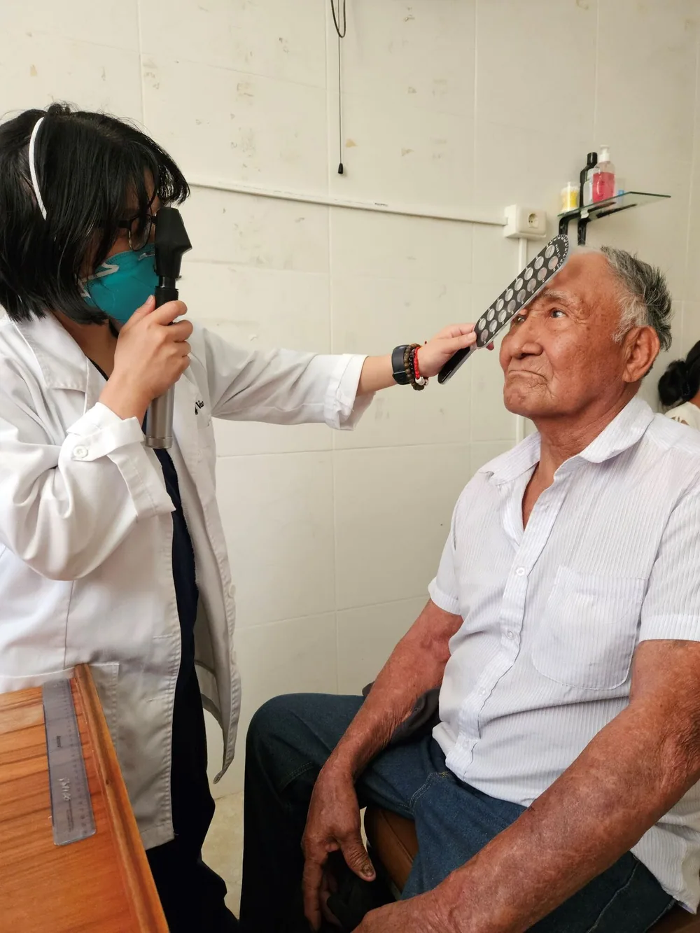 A clinician examines an older adult patient's eye during a vision screening.